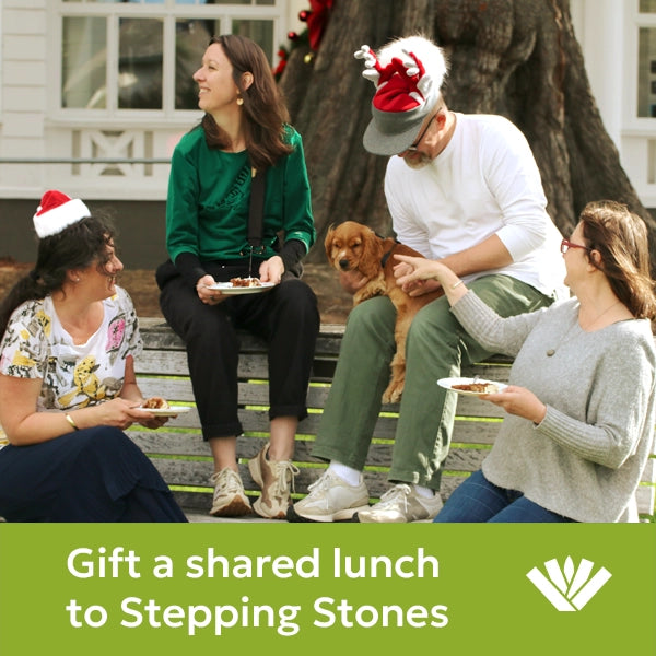 Four people sitting on a bench with a dog, wearing Santa hats, with text ' gift a shared lunch to Stepping Stones'
