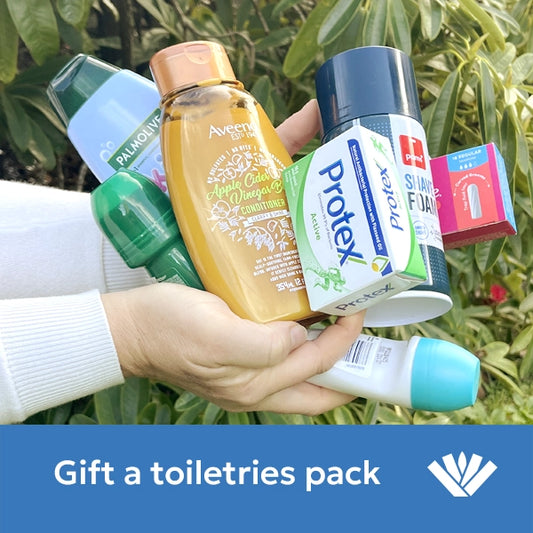 Hand holding various toiletries with a green leafy background and 'Gift a toiletries pack' text.