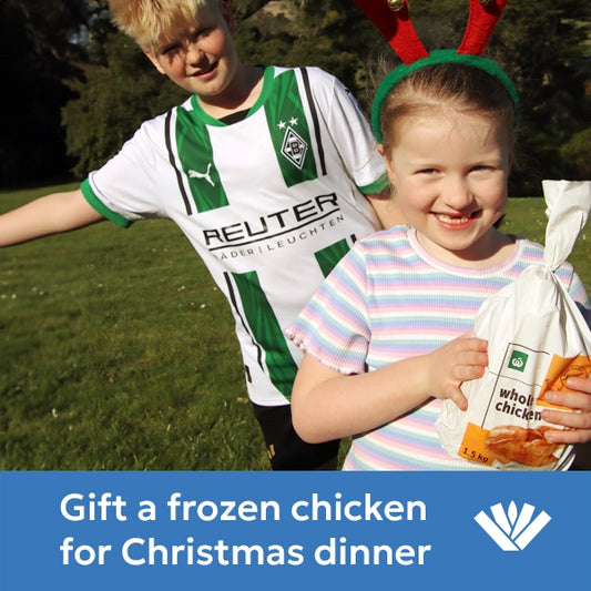 Two children outdoors, one holding a  frozen chicken with text gift a frozen chicken for Christmas dinner.